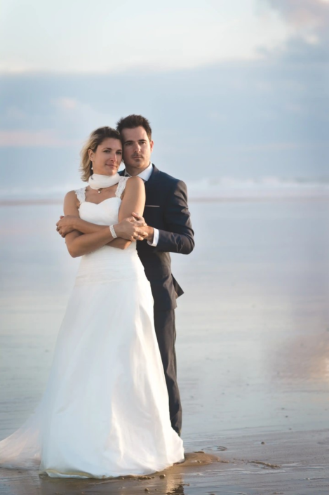 Couple de mariés enlacé sur une plage de Bordeaux, immortalisé dans un portfolio de photographe de mariage.