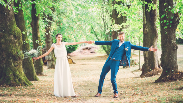 Couple de jeunes mariés rayonnants posant dans un parc arboré, incarnant la joie et l'amour du jour de leur mariage.