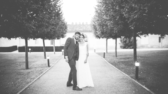 Couple de jeunes mariés se tenant par la main en noir et blanc, chemin bordé d'arbres, par lafocaledolga, photographe mariage à Bordeaux.