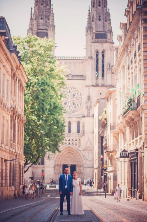 Un couple nouvellement marié se tient main dans la main devant la cathédrale Pey-Berland à Bordeaux, capturé par lafocaledolga.
