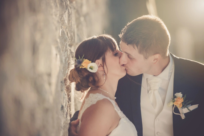 Photographe de mariage à Bordeaux capturant un baiser intime entre les mariés, avec une lumière arrière douce pour une ambiance romantique.