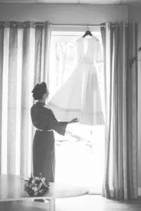Mariée contemplative devant sa robe de mariage suspendue, un moment intime en Gironde, immortalisé par lafocaledolga.