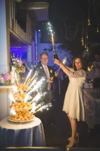 Un couple lors d'une soirée de mariage célébrant avec une bouteille de champagne scintillante à côté d'une table de desserts élégante.